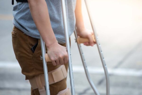 Disability Insurance - Close-up of Woman’s Lower Body and Knee Support Using Crutches Standing and Trying to Walk after Suffering a Work Related Injury