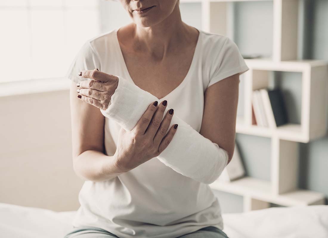 Group Accident Insurance - Close-up of a Female Sitting with a Broken Arm in a Plaster Cast in a Hospital Patient Room and Holding Her Injured Arm with Her Other Hand for Support