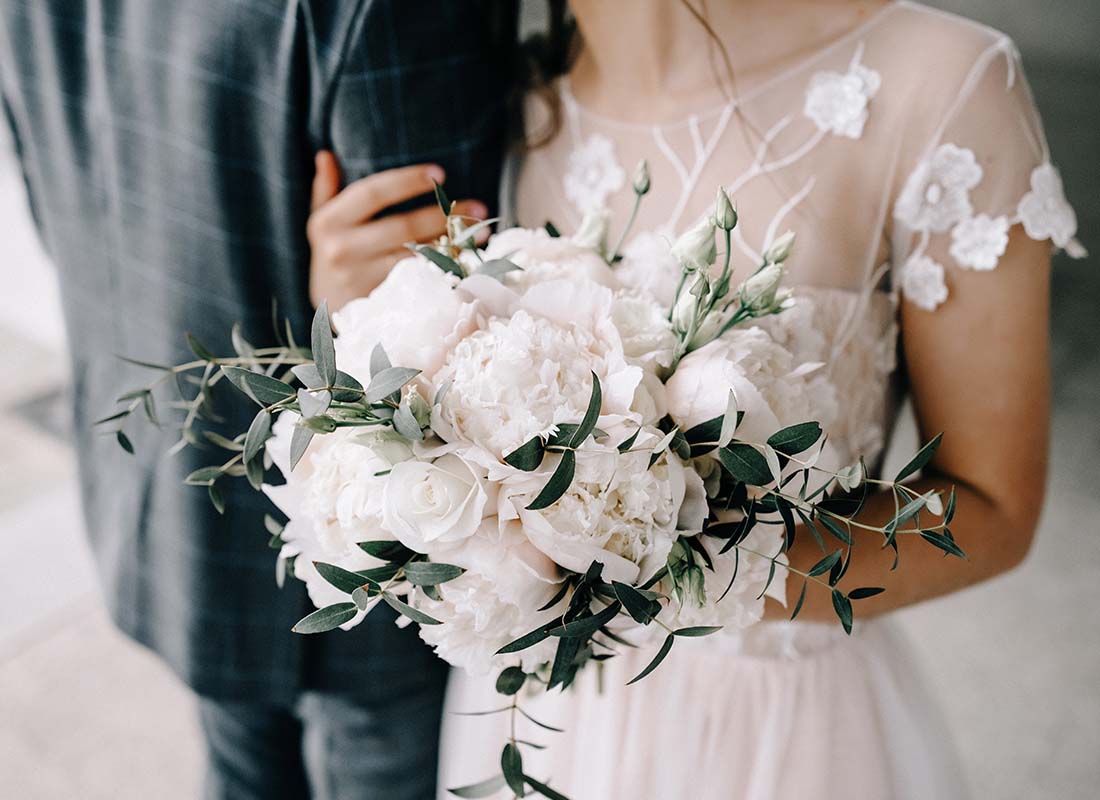 Wedding-Insurance-Close-up-of-a-Bouquet-in-a-Brides-Hands-While-She-is-Holding-the-Arm-of-the-Groom-After-the-Wedding-Ceremony